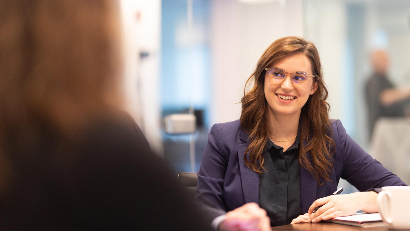 A woman sits in a conference room and chats with a colleague